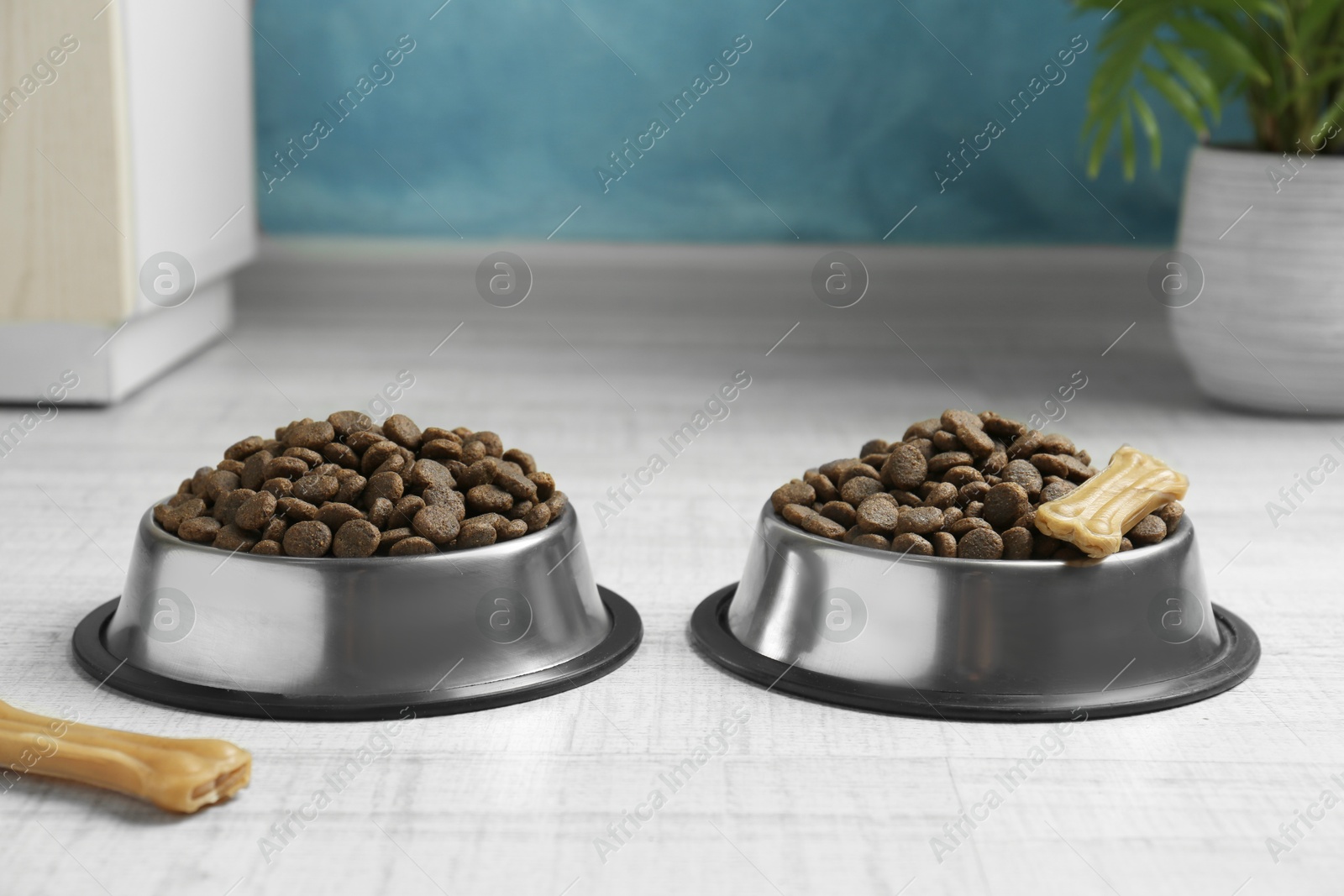 Photo of Dry pet food in feeding bowls and chew bones on floor indoors