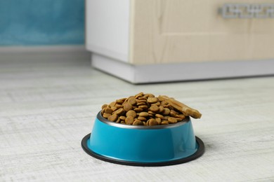 Photo of Dry pet food in feeding bowl and chew bone on floor indoors