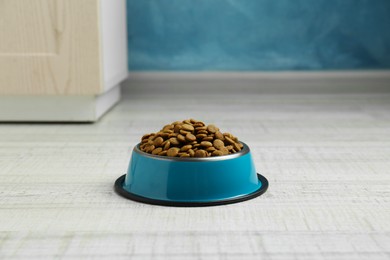 Photo of Dry pet food in feeding bowl on floor indoors