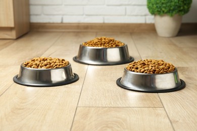 Photo of Dry pet food in feeding bowls on floor indoors