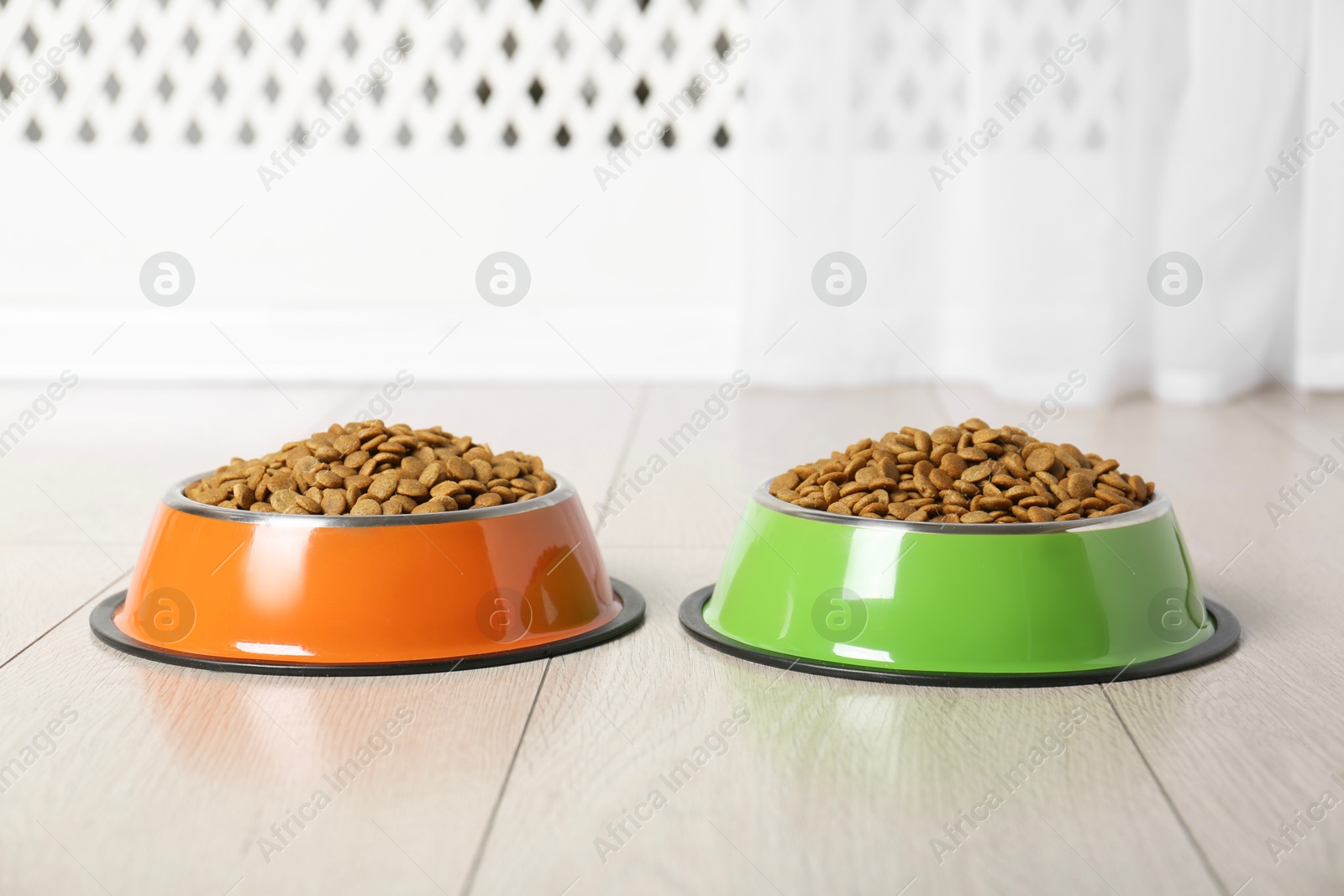 Photo of Dry pet food in feeding bowls on floor indoors