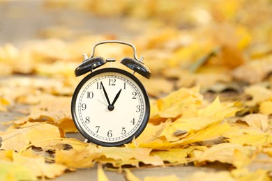 Photo of Autumn time. Alarm clock and fallen leaves on pathway outdoors, closeup