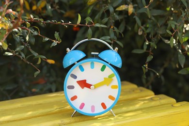 Photo of Autumn time. Alarm clock on bench outdoors, closeup