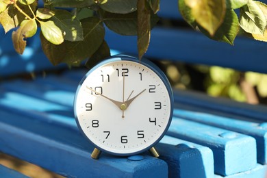 Photo of Autumn time. Alarm clock on bench outdoors, closeup