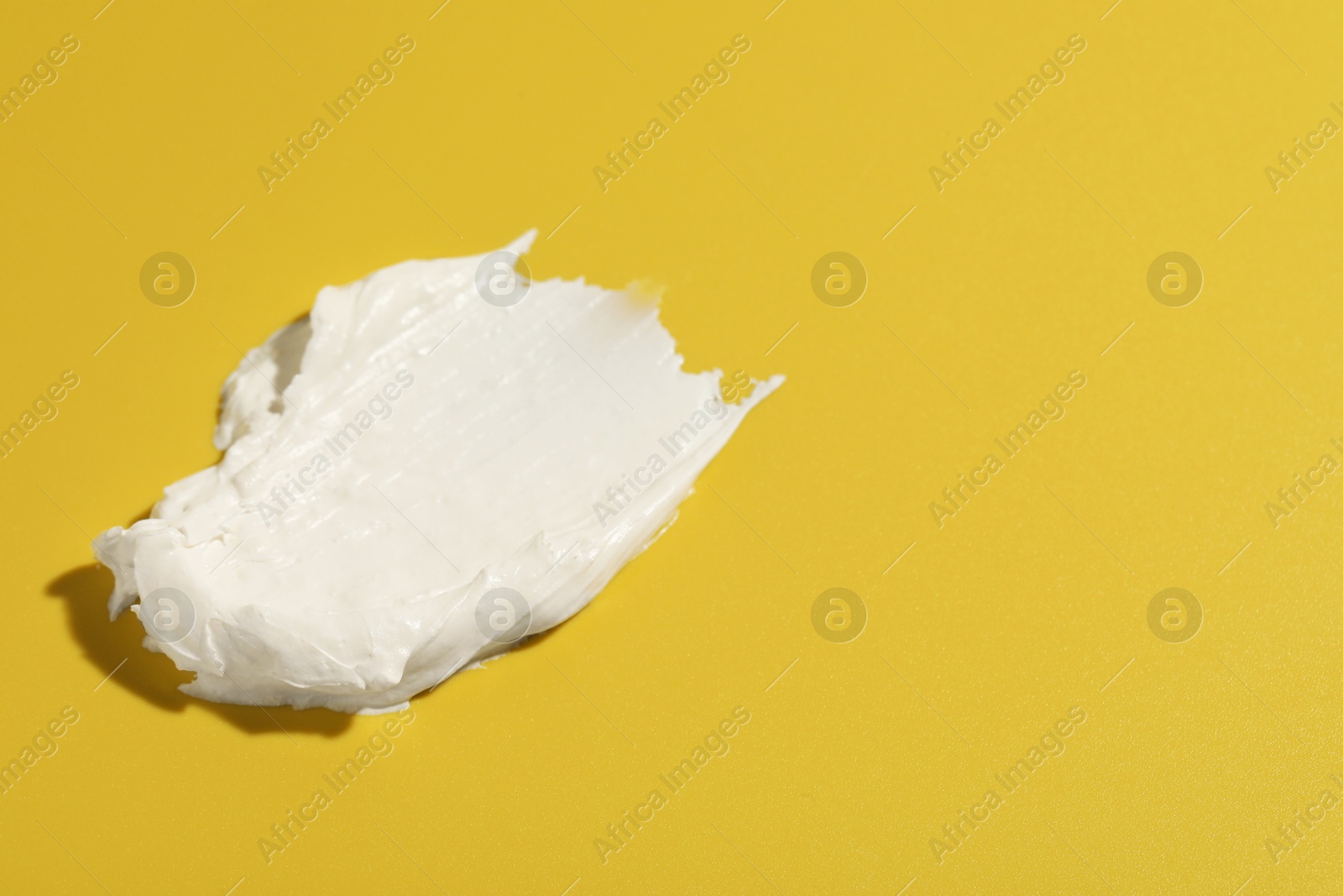 Photo of Cream on dark yellow background, closeup. Sample of cosmetic product