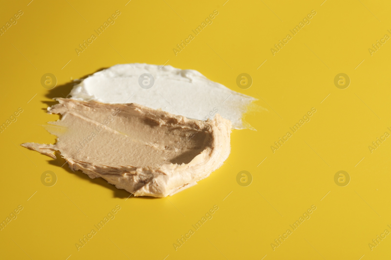 Photo of Samples of cream on dark yellow background, closeup. Space for text