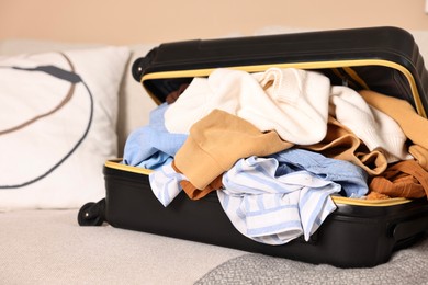 Photo of Open suitcase full of different messy clothes on sofa indoors