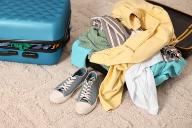 Photo of Suitcase with pile of different messy clothes, another one and sneakers on carpet