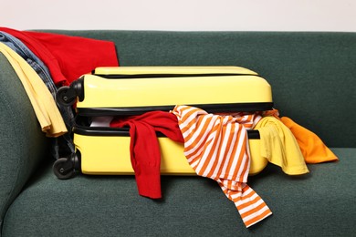 Photo of Bright suitcase full of different messy clothes on sofa indoors
