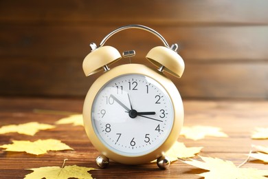 Photo of Autumn time. Alarm clock and golden leaves on wooden table