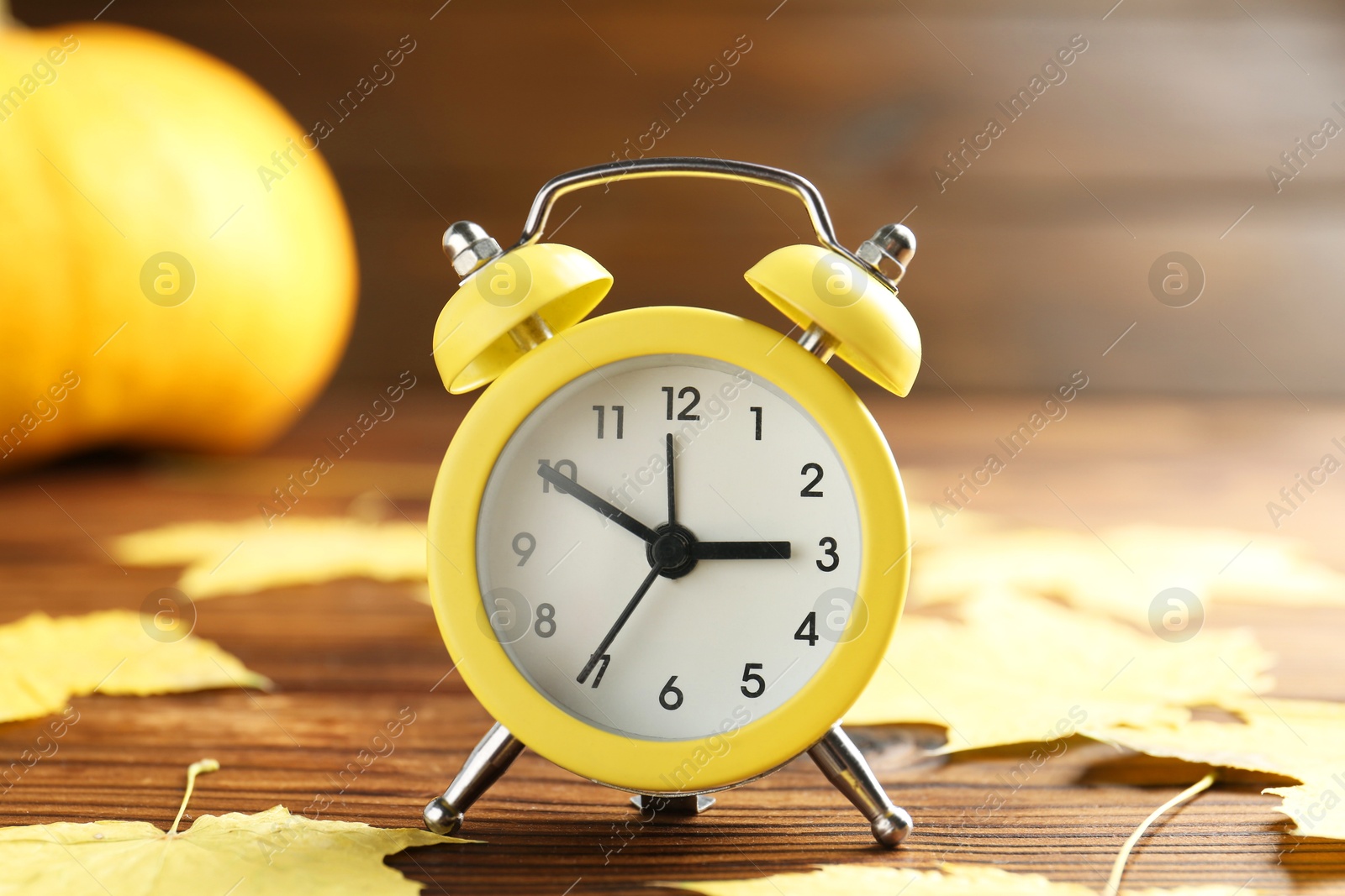 Photo of Autumn time. Alarm clock and golden leaves on wooden table