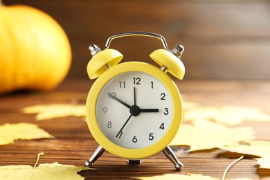 Photo of Autumn time. Alarm clock and golden leaves on wooden table