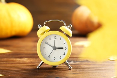 Photo of Autumn time. Alarm clock and golden leaves on wooden table