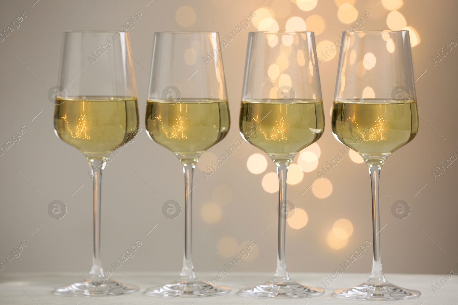 Photo of Tasty white wine in glasses on table against grey background with blurred lights, bokeh effect