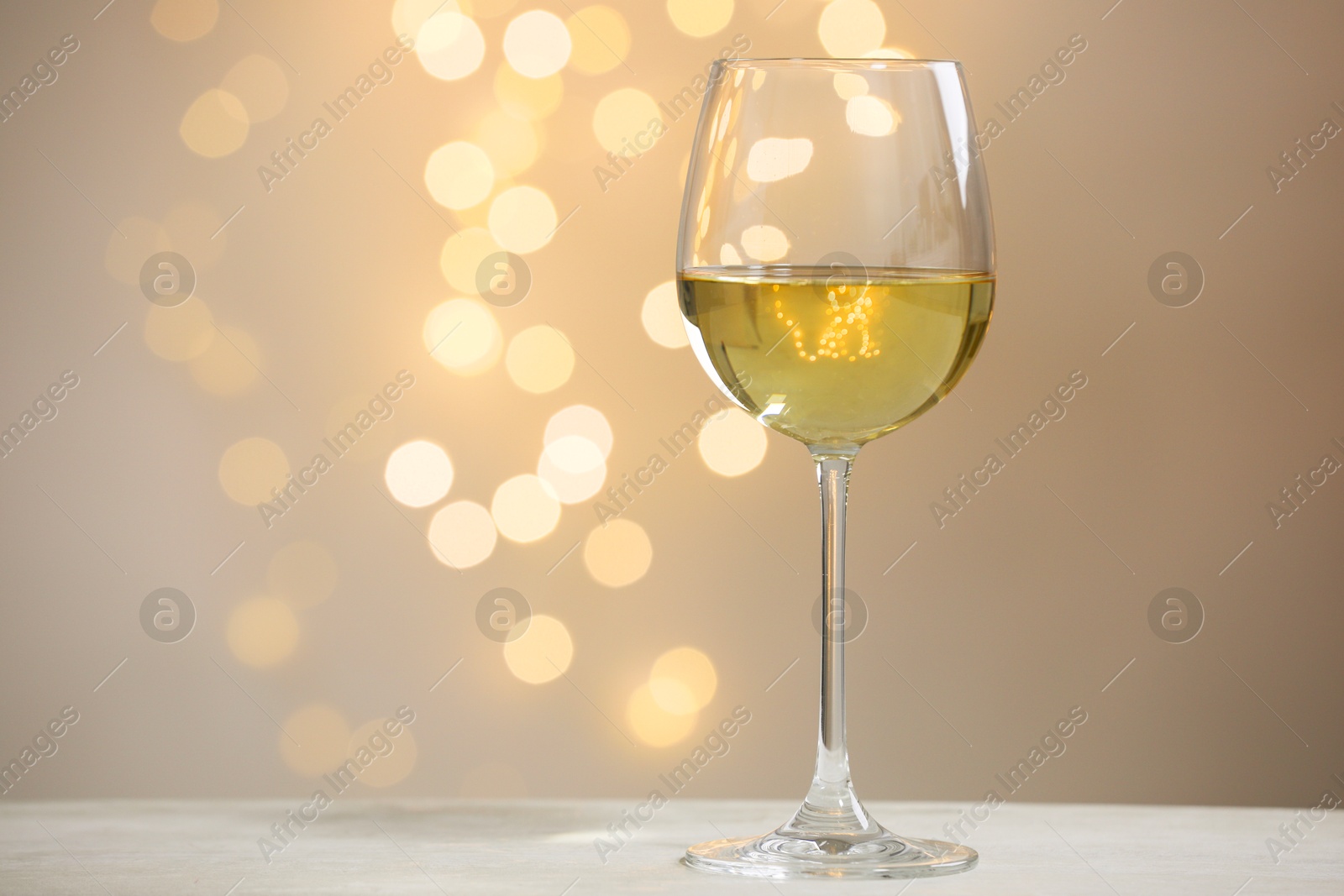 Photo of Tasty white wine in glass on table against grey background with blurred lights, bokeh effect. Space for text