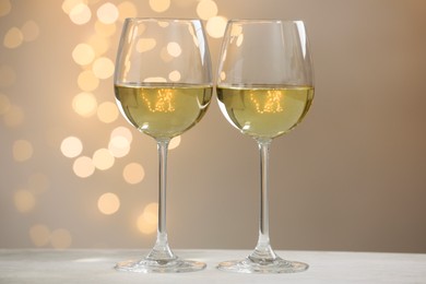 Photo of Tasty white wine in glasses on table against grey background with blurred lights, bokeh effect