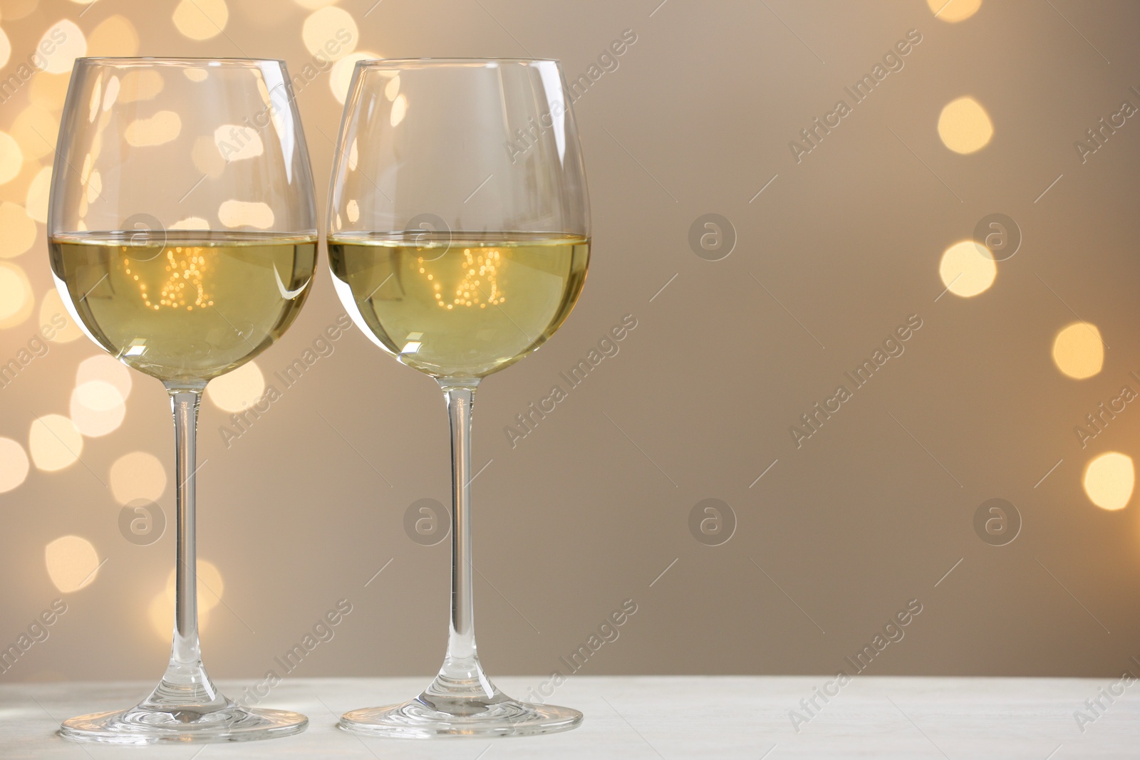 Photo of Tasty white wine in glasses on table against grey background with blurred lights, bokeh effect. Space for text