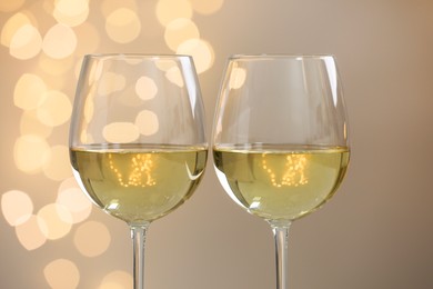 Photo of Tasty white wine in glasses against grey background with blurred lights, closeup. Bokeh effect