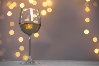 Photo of Tasty white wine in glass on table against grey background with blurred lights, bokeh effect. Space for text