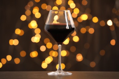 Photo of Tasty red wine in glass on table against dark background with blurred lights, bokeh effect