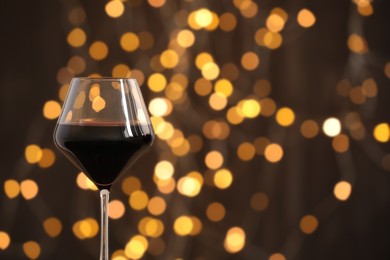 Photo of Tasty red wine in glass against dark background with blurred lights, closeup. Bokeh effect