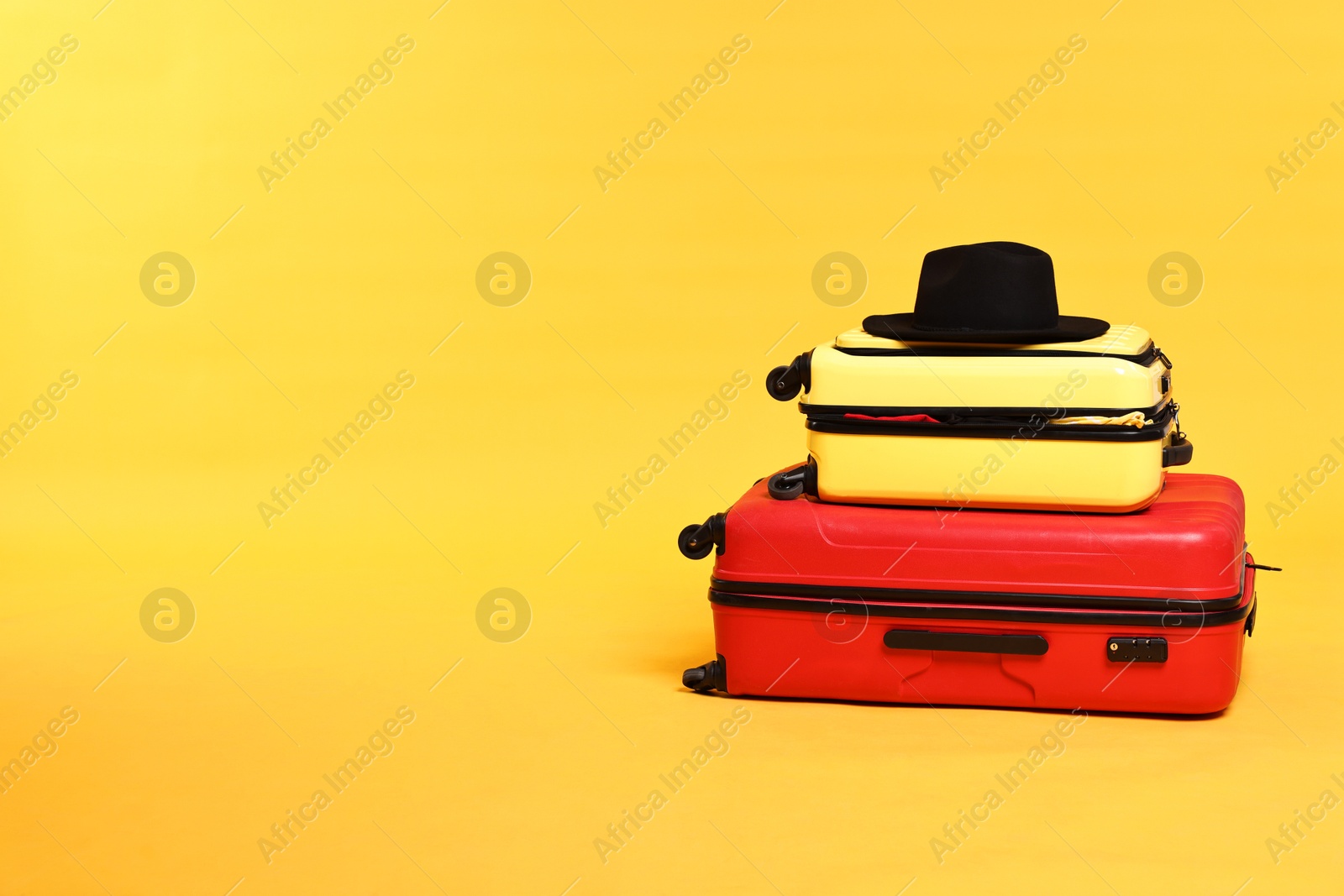 Packed suitcases and hat on yellow background. Space for text Photo of Packed suitcases and hat on yellow background. Space for text