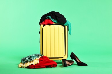 Photo of Suitcase, messy clothes and shoes on green background