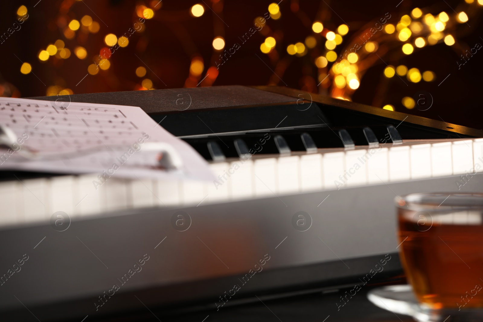 Photo of Piano with musical notes, earphones and cup of tea on table against blurred lights, closeup. Bokeh effect