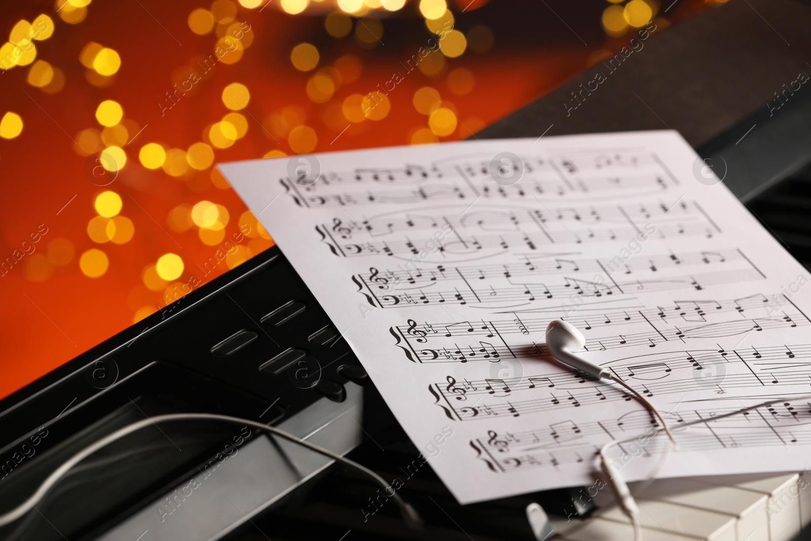 Photo of Sheet with musical notes and earphones on piano against blurred lights, closeup. Bokeh effect