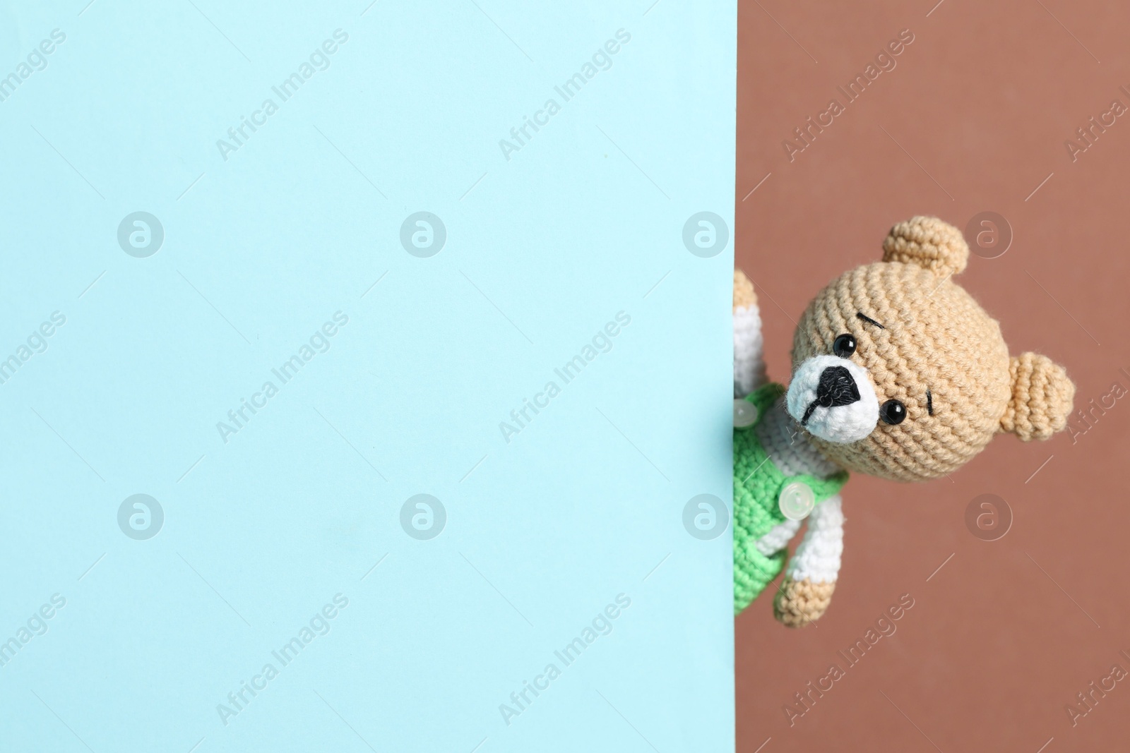 Photo of Cute toy bear peeking out of blank card on brown background. Space for text