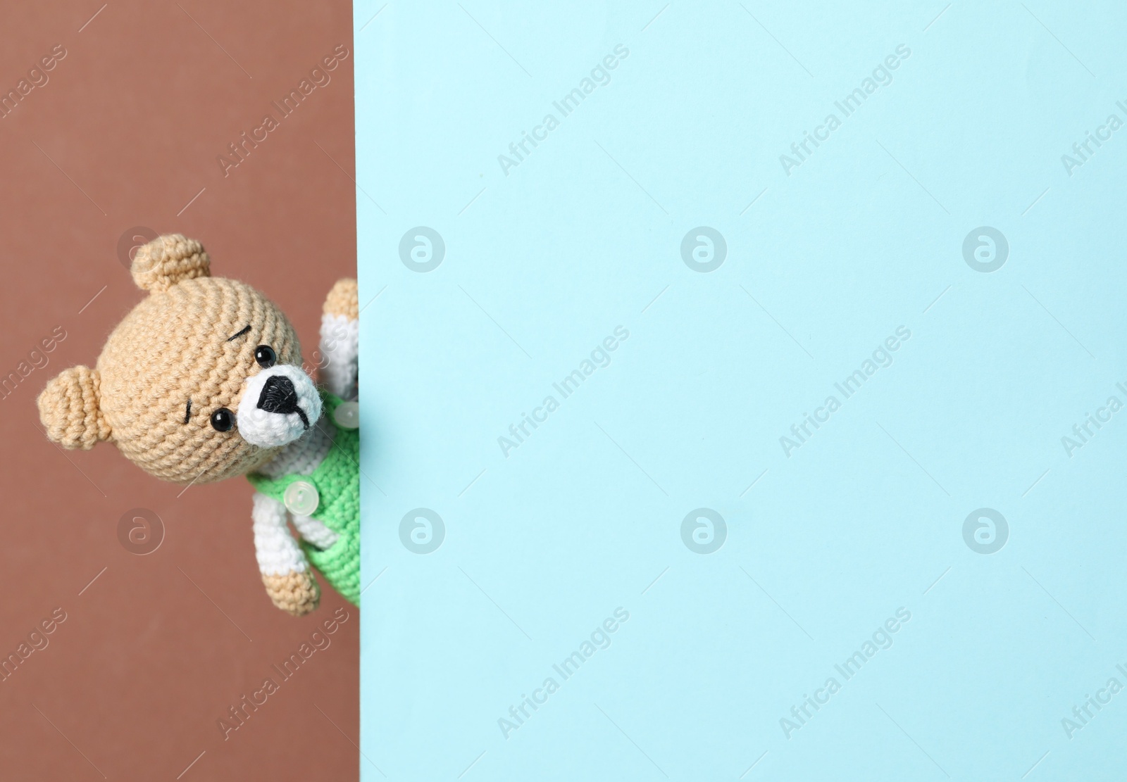 Photo of Cute toy bear peeking out of blank card on brown background. Space for text