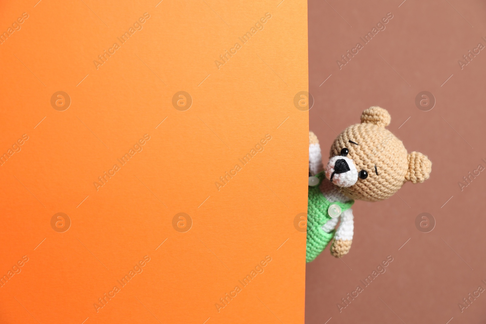 Photo of Cute toy bear peeking out of blank card on brown background. Space for text