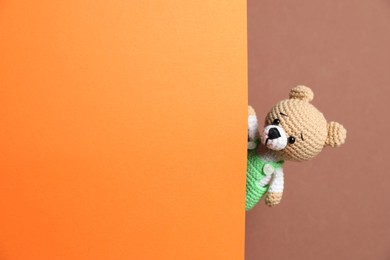 Photo of Cute toy bear peeking out of blank card on brown background. Space for text