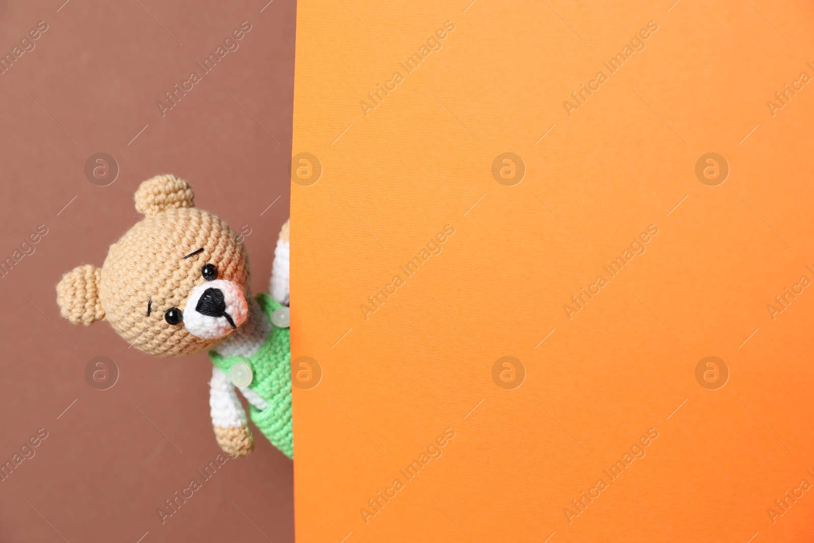 Photo of Cute toy bear peeking out of blank card on brown background. Space for text