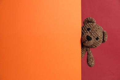 Photo of Cute toy bear peeking out of blank card on red background. Space for text