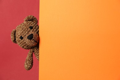 Photo of Cute toy bear peeking out of blank card on red background. Space for text