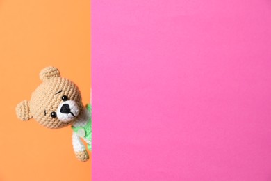 Photo of Cute toy bear peeking out of blank card on orange background. Space for text