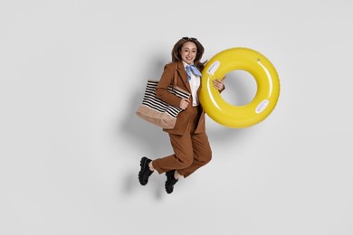 Photo of Businesswoman with inflatable ring, bag and sunglasses jumping on white background