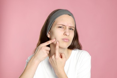 Photo of Upset teenage girl popping pimple on her face against pink background. Acne problem