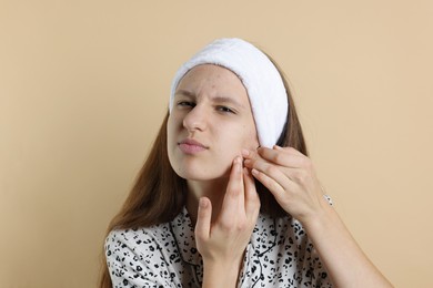 Photo of Upset teenage girl popping pimple on her face against beige background. Acne problem