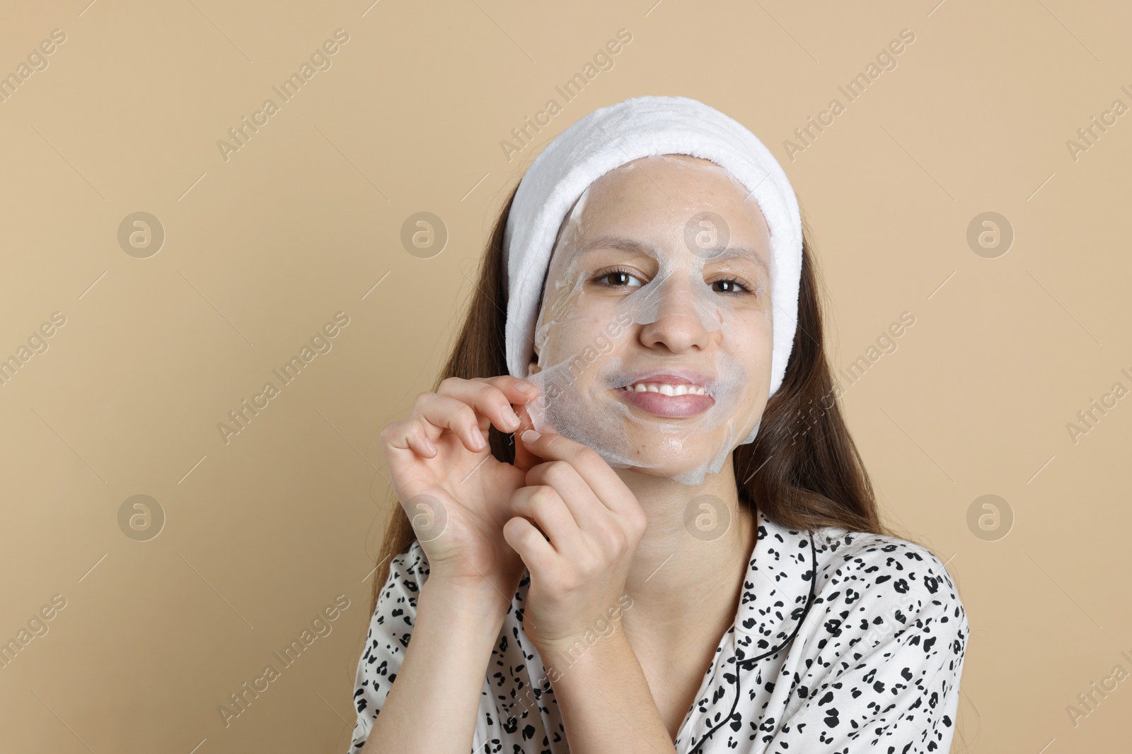 Photo of Teenage girl removing sheet facial mask on beige background. Acne treatment