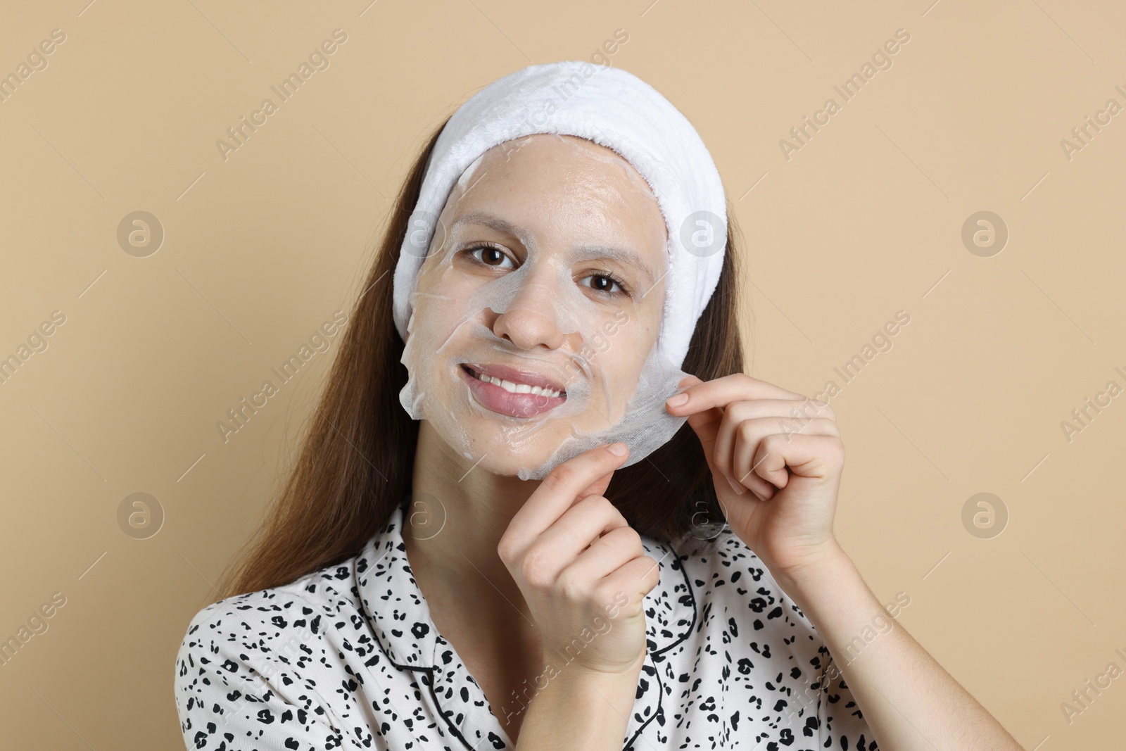 Photo of Teenage girl removing sheet facial mask on beige background. Acne treatment