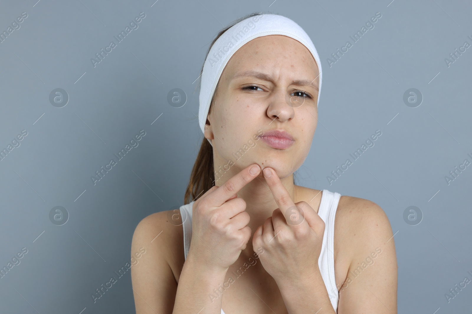 Photo of Upset teenage girl popping pimple on her face against grey background. Acne problem