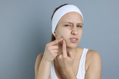 Photo of Upset teenage girl popping pimple on her face against grey background. Acne problem