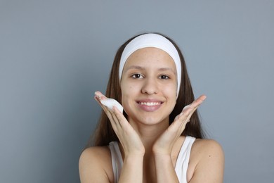 Photo of Teenage girl with acne problem applying cleansing foam on grey background