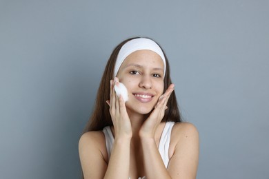 Photo of Teenage girl with acne problem applying cleansing foam on grey background