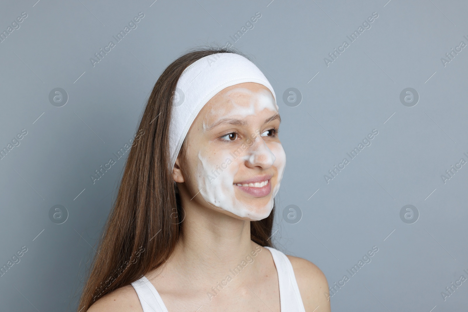 Photo of Teenage girl with cleansing foam on her face against grey background, space for text. Acne treatment