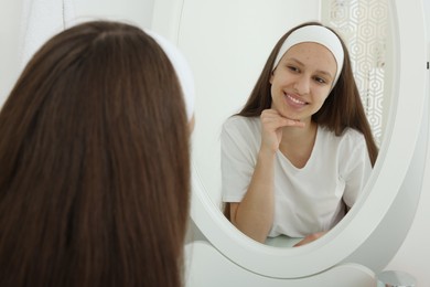 Photo of Teenage girl with acne problem looking in mirror indoors