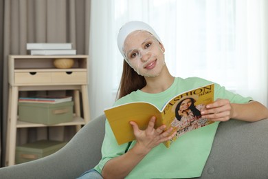 Photo of Teenage girl with sheet facial mask reading magazine at home. Acne treatment