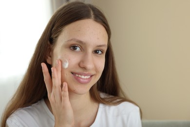 Photo of Teenage girl applying cream onto face at home, space for text. Acne treatment